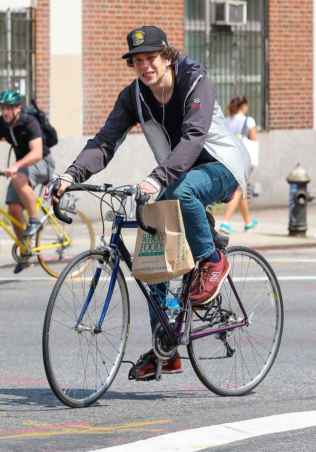 Ein Mann mit einer Golden State Warriors-Kappe fährt mit einer Tüte von Whole Foods auf dem Fahrrad.