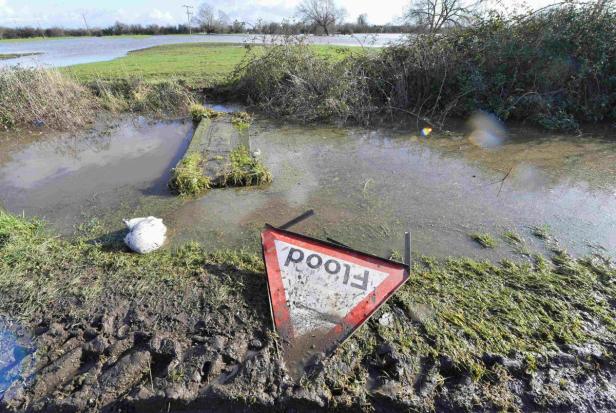 Ein umgefallenes Warnschild „Flood“ (Überschwemmung) steht in einem überfluteten Gebiet.