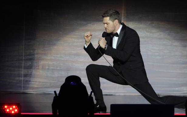 Michael Bublé kniet während eines Auftritts auf der Bühne und singt in ein Mikrofon.