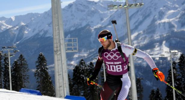 Ein Biathlet mit Startnummer 108 läuft auf Skiern vor einer Bergkulisse.