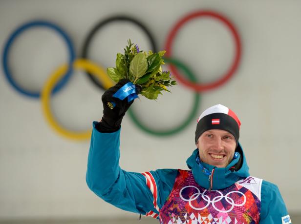 Ein österreichischer Athlet hält einen Blumenstrauß vor dem Hintergrund der olympischen Ringe.