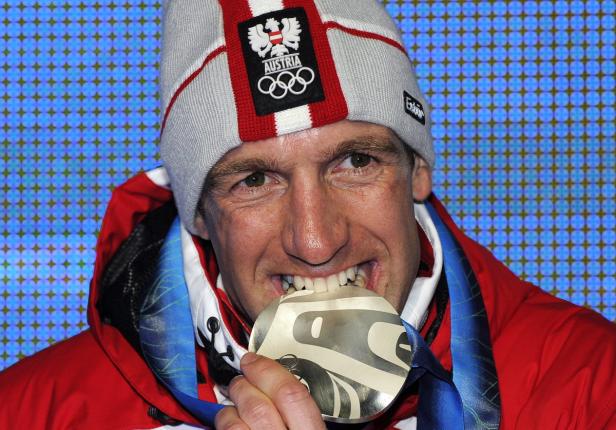 Ein österreichischer Athlet beißt in seine olympische Goldmedaille.