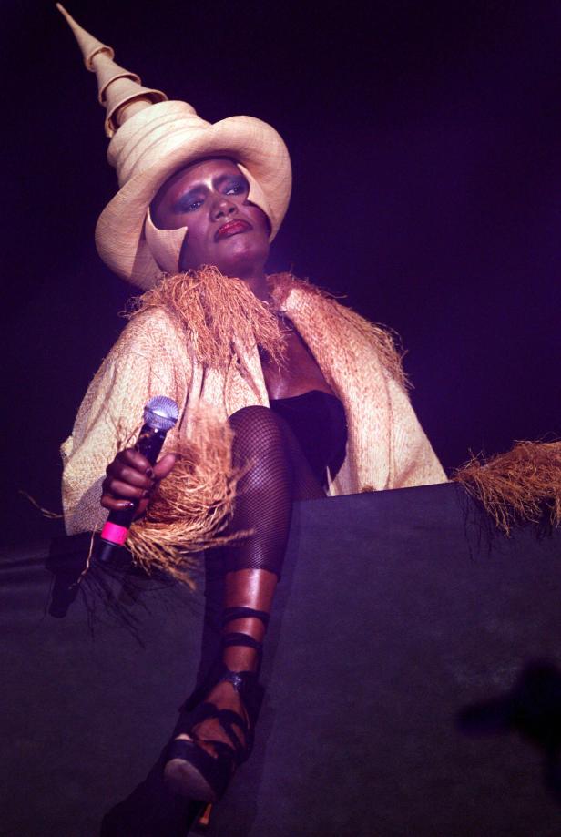 Grace Jones mit einem extravaganten Hut und einem Mikrofon in der Hand.