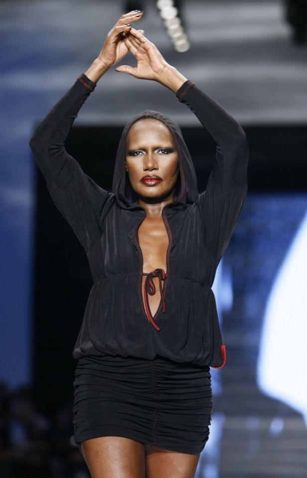Grace Jones posiert in einem schwarzen Kapuzenkleid auf einem Laufsteg.