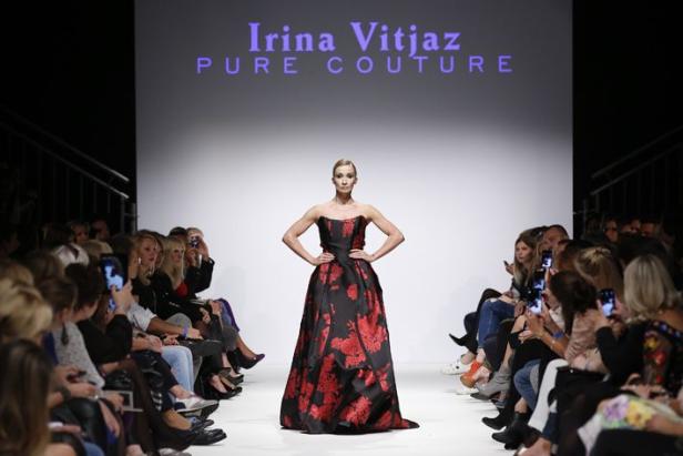 Eine Frau präsentiert ein schwarzes Abendkleid mit roten Blumen auf dem Laufsteg von Irina Vitjaz.