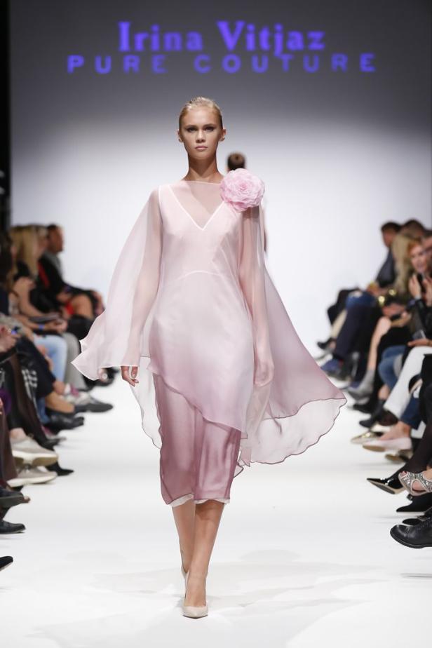 Ein Model präsentiert ein zartrosa Kleid mit einer großen Stoffblume auf dem Laufsteg.