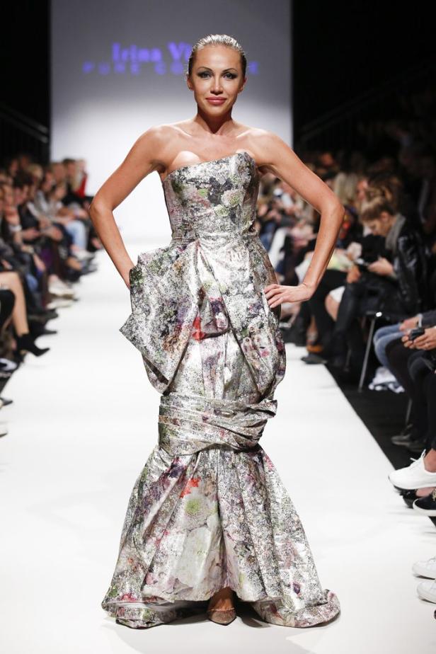 Ein Model präsentiert ein trägerloses, silbernes Kleid mit Blumenmuster auf dem Laufsteg.