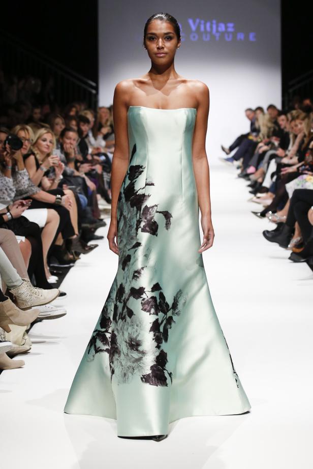 Eine Frau präsentiert ein trägerloses, hellblaues Abendkleid mit Blumenmuster auf dem Laufsteg.