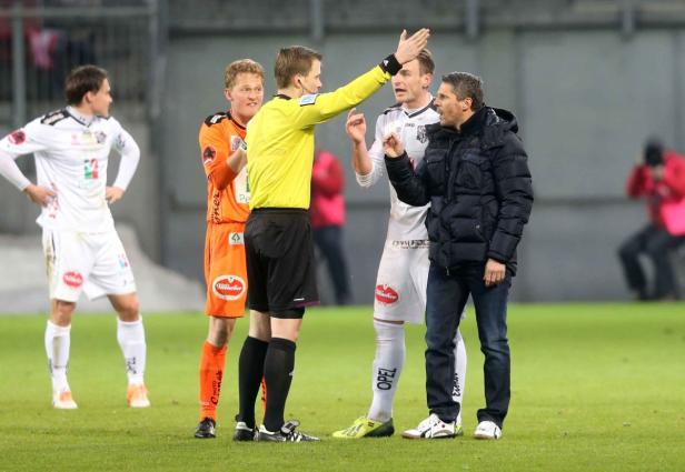 Ein Schiedsrichter diskutiert mit einem Trainer und zwei Fußballspielern auf dem Spielfeld.