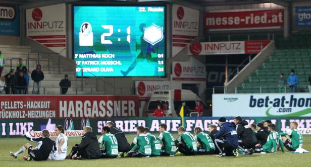 Fußballspieler sitzen nach dem Spiel auf dem Rasen, im Hintergrund eine Anzeigetafel mit dem Ergebnis 2:1.