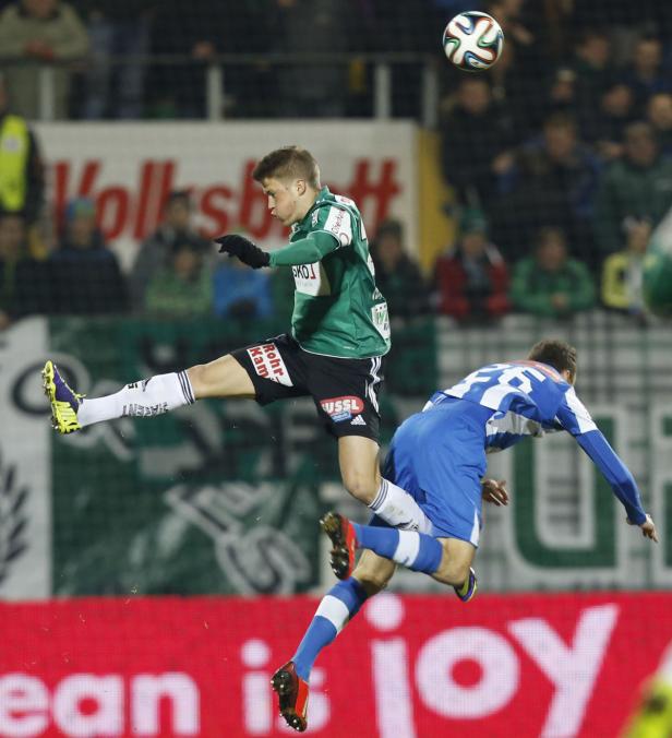 Ein Fußballspieler springt, um den Ball zu köpfen, während ein anderer Spieler zu Fall kommt.