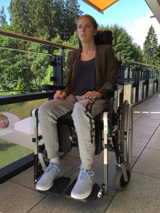 Eine junge Frau sitzt in einem Rollstuhl auf einer Terrasse.