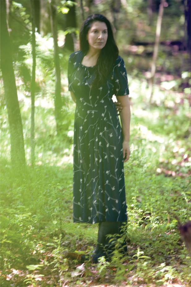 Eine Frau in einem geblümten Kleid steht in einem Wald.