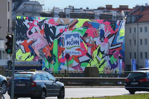Megaboard - Plakatstelle - Kampagne NÖM Echt Ein großes, farbenfrohes Wandbild mit einem Flamingo und dem Schriftzug „nöm“.