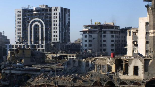 Zerstörte Gebäude und ein beschädigtes Hochhaus in einer Stadt.