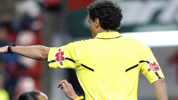 Ein Fußballschiedsrichter in gelbem Trikot zeigt eine Geste.
