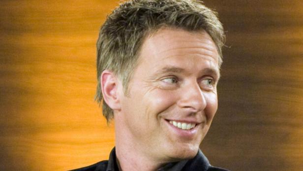 Ein lächelnder Mann mit blonden Haaren blickt zur Seite.