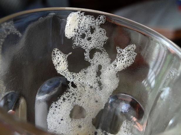 Schaumreste bilden eine Figur im Inneren eines Bierglases.