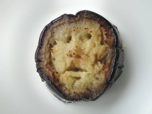 Eine Scheibe gebratene Aubergine liegt auf einem weißen Teller.