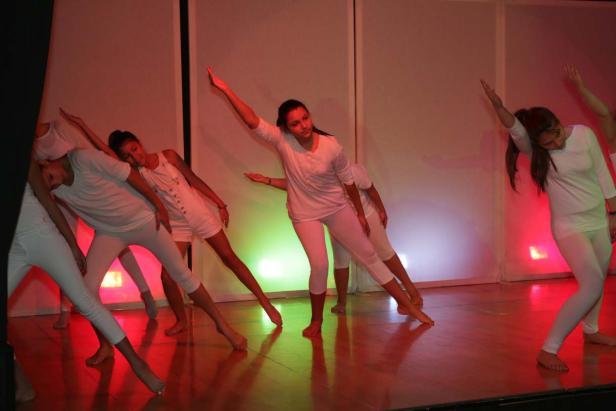 Eine Gruppe junger Tänzerinnen in weißen Kostümen führt eine synchrone Choreografie auf einer Bühne auf.