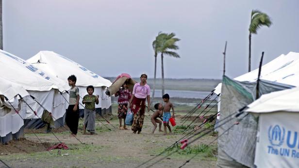 Eine Gruppe von Menschen steht vor Zelten in einem Flüchtlingslager.