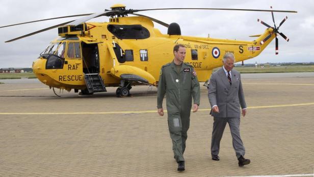 Prinz William und König Charles gehen vor einem gelben RAF-Rettungshubschrauber entlang.
