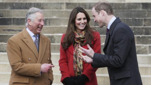 Prinz Charles, Prinzessin Kate und Prinz William stehen auf einer Treppe und lachen.