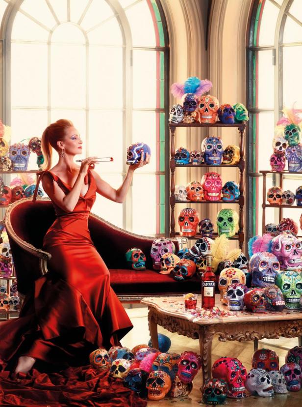 Eine Frau im roten Kleid sitzt auf einem Sofa, umgeben von bemalten Totenköpfen.
