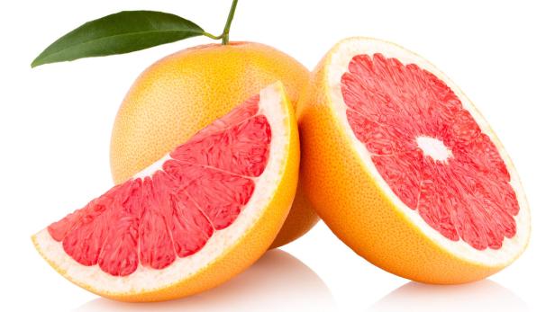 Eine ganze und zwei halbe, rosafleischige Grapefruits liegen auf einer weißen Fläche.