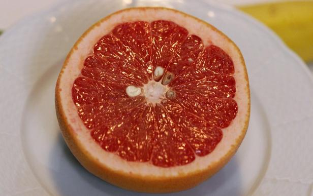 Eine halbe, rote Grapefruit liegt auf einem weißen Teller.