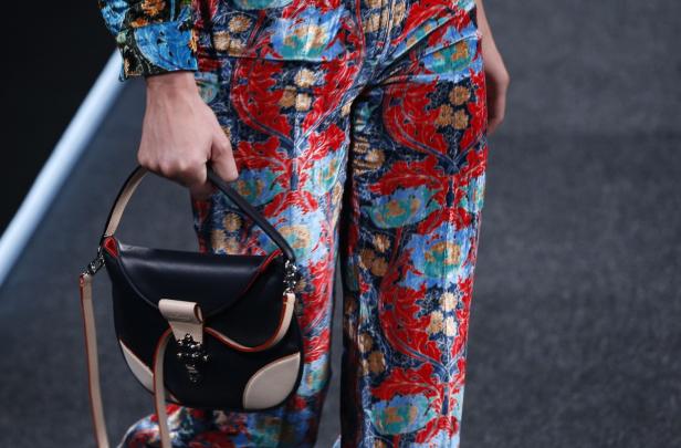Eine Person mit gemusterter Hose hält eine schwarze Handtasche.
