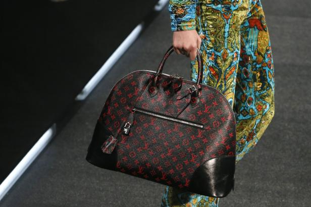 Eine Person trägt eine Louis Vuitton Tasche mit rotem Muster auf schwarzem Grund.