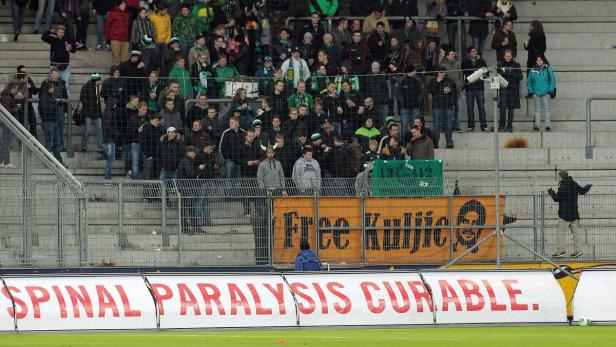 Zuschauer stehen auf einer Tribüne in einem Fußballstadion.
