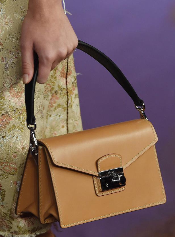 Eine Person hält eine hellbraune Ledertasche mit schwarzem Griff.