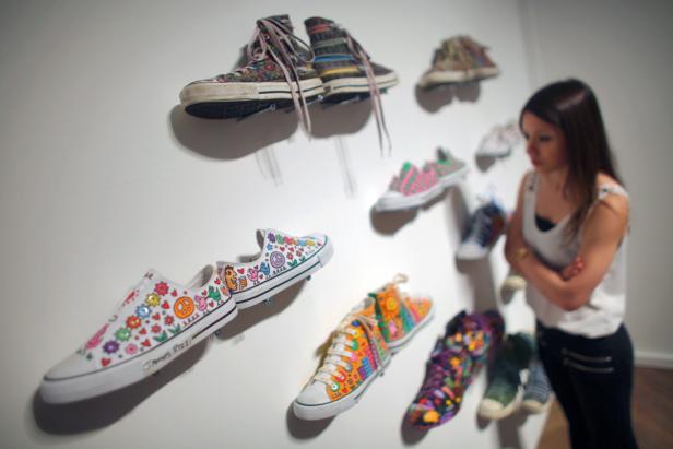 Eine Frau betrachtet eine Ausstellung von bemalten Turnschuhen an einer Wand.