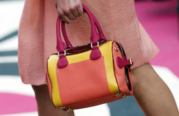 Eine Person trägt eine farbenfrohe Handtasche in Gelb, Orange und Pink.