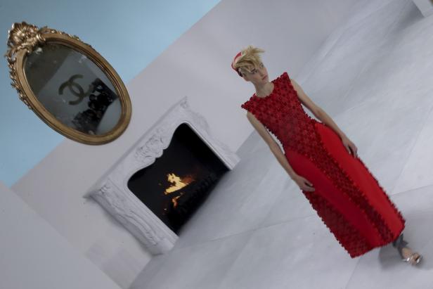 Ein Model in einem roten Kleid von Chanel steht vor einem Kamin und einem Spiegel mit dem Chanel-Logo.
