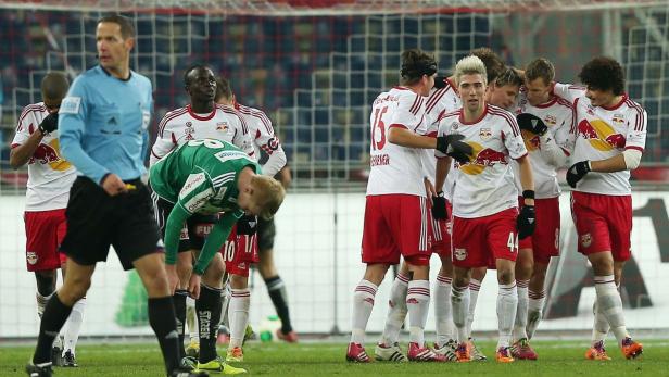 Fußballspieler von RB Salzburg feiern auf dem Spielfeld, während ein Gegenspieler sich krümmt.