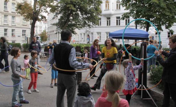 Eine Gruppe von Kindern und Erwachsenen spielt mit Hula-Hoop-Reifen auf einer Straße in der Stadt.