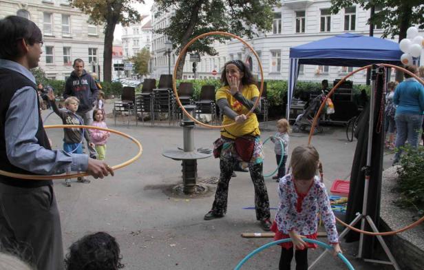 Eine Frau zeigt Kindern auf einem Platz, wie man Hula-Hoop macht.