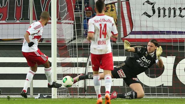 Ein Fußballspieler schießt einen Ball auf das Tor, während der Torwart versucht, ihn abzuwehren.