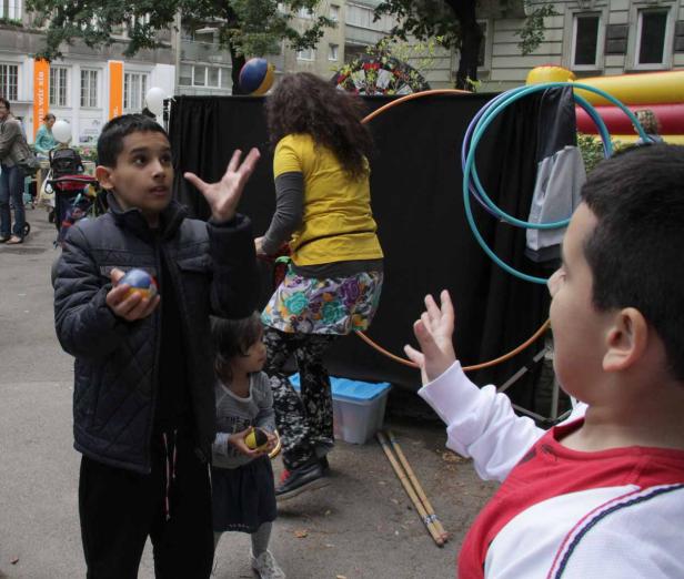 Kinder üben sich im Jonglieren mit Bällen und Reifen auf einer Straße.