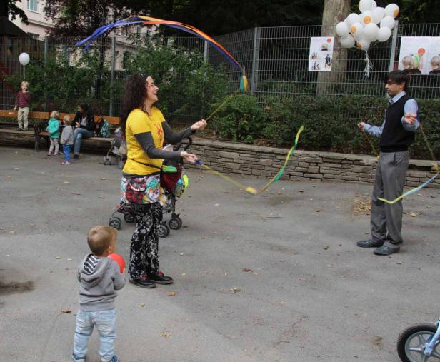 Eine Frau und ein Mann spielen mit bunten Bändern mit Kindern im Park.
