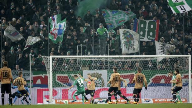 Fußballspieler in Grün und Gelb kämpfen vor einem Tor, während Fans zusehen.