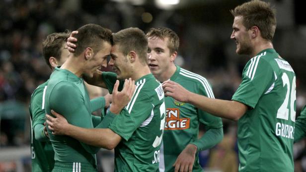 Eine Gruppe von Fußballspielern in grünen Trikots umarmt sich und feiert.