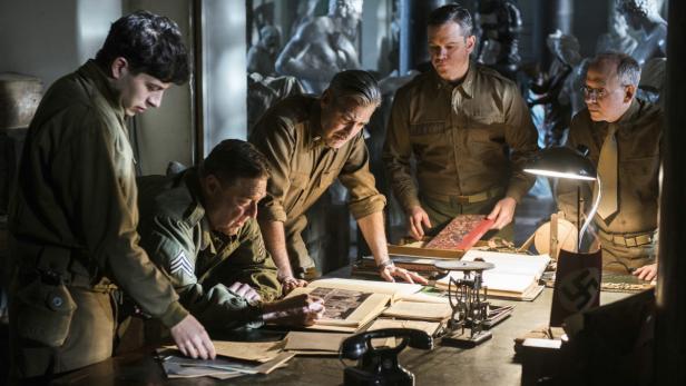 Eine Gruppe von Soldaten, darunter George Clooney und Matt Damon, betrachtet Dokumente an einem Tisch mit Hakenkreuzflagge.