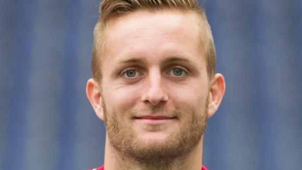 Porträt eines Mannes mit blonden Haaren und Bart vor einem blauen Hintergrund.