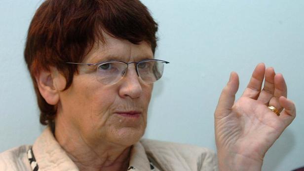 Eine ältere Frau mit Brille gestikuliert mit ihrer Hand.