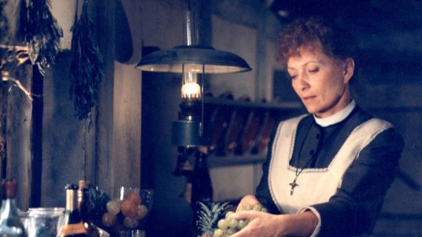 Eine Frau in Tracht arrangiert Obst unter dem Licht einer Lampe.