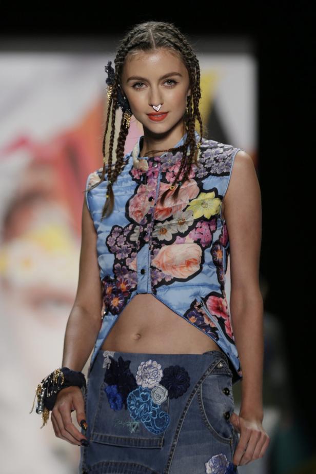 Ein Model mit Zöpfen und Nasenring präsentiert ein blaues, florales Top und einen Jeansrock.